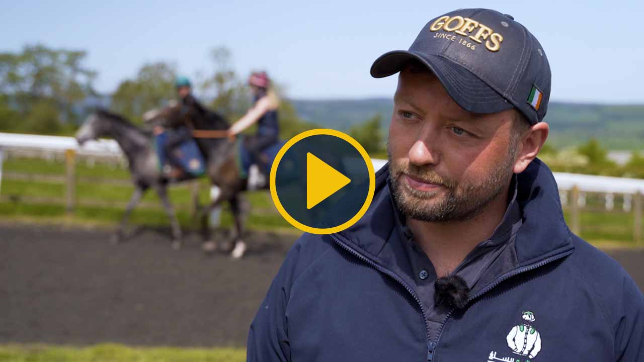 Horse racing trainer with horses in the background on a training track